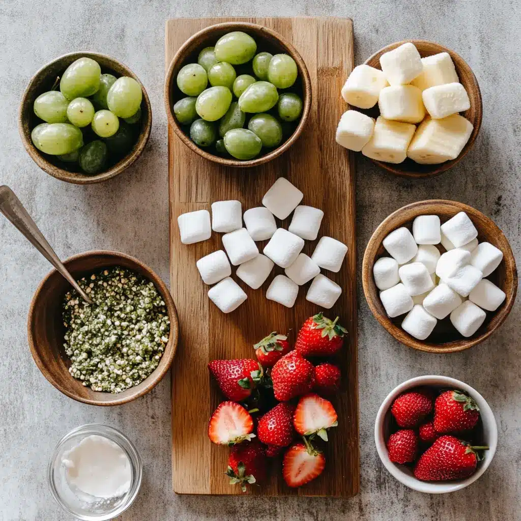 Grinch Kabobs for a Vibrant Christmas Celebration 3 Vibrant Grinch Kabobs ingredients, including green grapes, strawberries, banana slices, and mini marshmallows, ready for assembly on a clean surface.