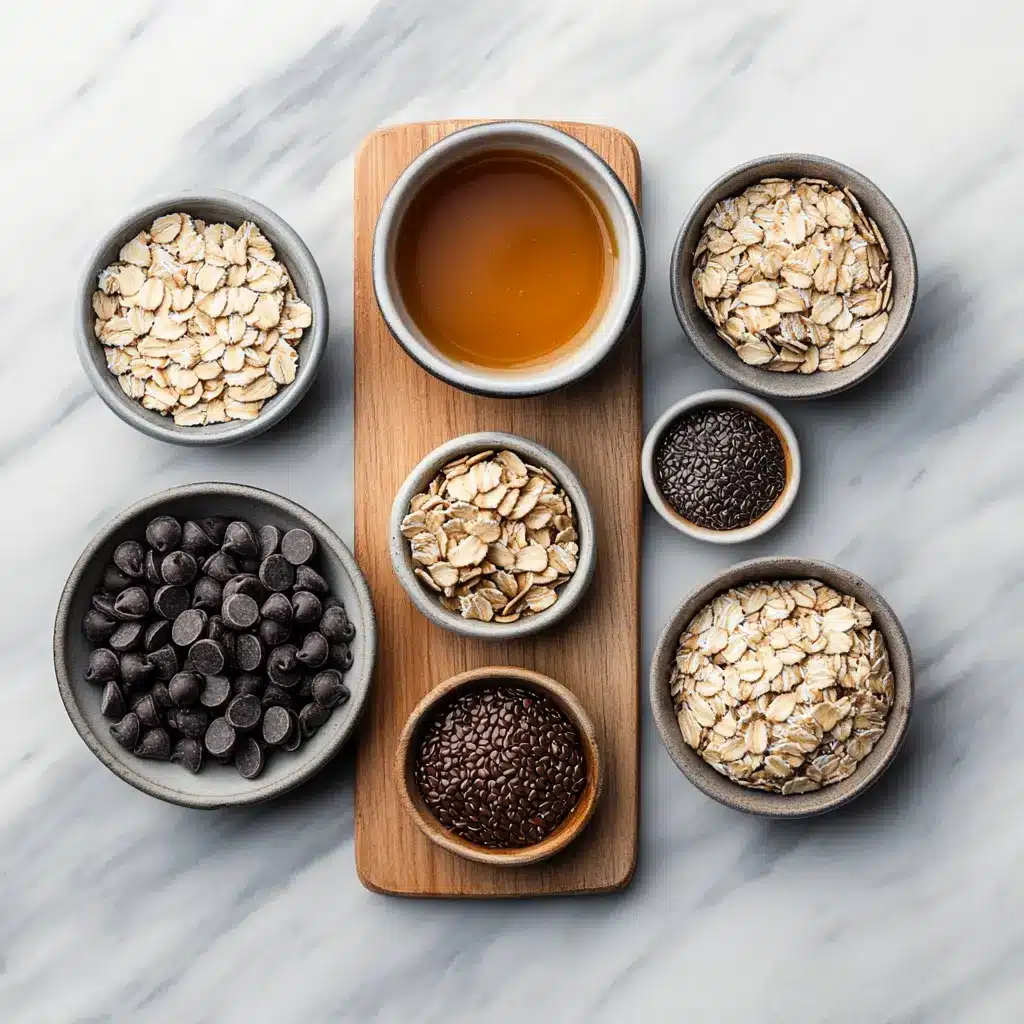 A flat lay of ingredients for no-bake peanut butter energy balls: rolled oats, creamy peanut butter, ground flaxseed, mini chocolate chips, and maple syrup.